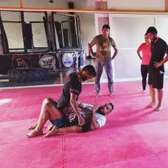 Here, two students are drilling a guard pass. This exercise teaches the person on top how to navigate their opponent's legs to gain a more dominant position, a key aspect of grappling.