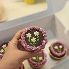 Holding up one of my floral cupcakes. This design features delicate, hand-piped daisies on a rich chocolate ganache base, framed by a purple buttercream border.