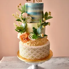 This four-tiered wedding cake combines multiple intricate techniques. The base features a gold filigree stencil, leading up to hand-painted watercolor effects and a cascade of handmade sugar flowers, all encasing a rich chocolate ganache.