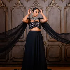A dramatic full-length portrait in a black lehenga with a flowing cape. The grand, traditional backdrop in my studio contrasts beautifully with the modern, edgy outfit.