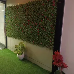 This office or commercial lobby features a lush green wall with hints of red flowers, paired with an artificial turf floor. It creates a vibrant and welcoming atmosphere for employees and visitors.