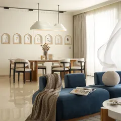 The living area flows seamlessly into the dining space, united by a shared language of soft curves and minimalist elegance. A deep blue sofa provides a gentle anchor, while the custom-shaped marble dining table reflects the home's organic and inviting character.