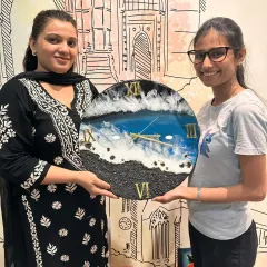 A student and I pose with her completed resin art clock, a beautiful piece that captures the movement of ocean waves against a shore.
