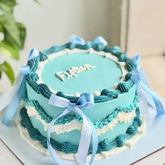 Fifteen, but make it vintage. This custom cake features intricate buttercream piping in shades of teal and white, adorned with delicate sheer and satin ribbons for a dreamy, balletcore-inspired look.