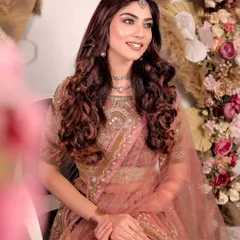 A smiling portrait of a model in the dusty pink and gold lehenga. The soft curls and delicate jewellery create a romantic look perfect for an engagement photoshoot.