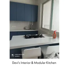 A simple and elegant kitchen in Andheri with matte blue cabinets and a clean white countertop that doubles as a breakfast bar. The large window provides excellent ventilation and natural light.