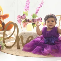 Waving hello to being one year old. This adorable shot captures the excitement of a first birthday, complete with a "One" sign and a festive, floral tea party theme.