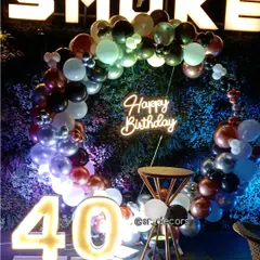 This 40th birthday setup at a restaurant features a multi-colored balloon ring against a green wall, a neon sign, and large marquee numbers.