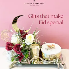 This Eid hamper is all about serene elegance. A mirrored tray holds a scented candle and a box of treats, beautifully arranged with white and red roses and a golden crescent moon accent.