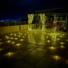 A rooftop cabana setup against the night sky. The combination of the warm LED candles on the floor and the twinkling lights of the cabana creates an incredibly romantic atmosphere.