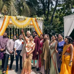 A joyous moment with family and friends right after the ceremony. The outdoor mandap, decorated with yellow and white florals, provides a bright and cheerful backdrop for group photos.