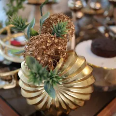 Our sculptural golden vase with a swirl design, holding a small floral arrangement. This piece is more than a vase; it’s a work of art, designed to be a stunning centerpiece on any table.
