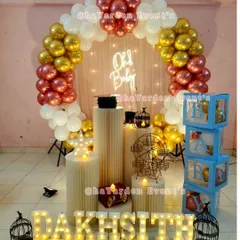 An elegant 'Oh Baby' setup with a balloon arch in rose gold, gold, and white. The decor is complete with pedestals, marquee letters, and 'BABY' blocks.