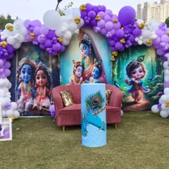 A closer look at the Krishna-themed baby shower setup on a lawn. The vibrant backdrop and purple and white balloon arch create a stunning visual against the open sky.