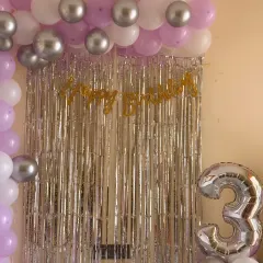 An elegant home setup for a 3rd birthday using a silver shimmer curtain with lavender and silver balloons. It's a simple way to make a milestone feel special without a big budget.