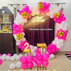 A vibrant pink and white circular balloon arch for a second birthday. This home setup includes a 'Happy Birthday' neon sign and the child's name in large light-up letters, creating a bright and cheerful photo spot.