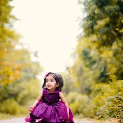 A beautiful portrait of Anaya in a purple dress, looking up with wonder during her outdoor birthday photoshoot.