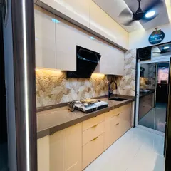 This parallel kitchen design creates a warm and luxurious feel with high-gloss beige cabinets and ambient lighting. Note the textured stone backsplash and integrated black chimney, creating a seamless and elegant workspace.