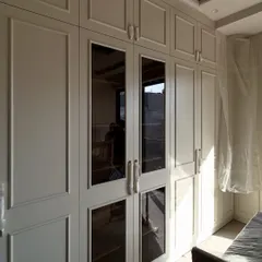 A view of the custom wardrobes during installation, showing the combination of solid and glass-paneled doors that provide both concealed and visible storage.