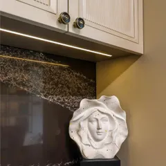 Art and function coexist beautifully in our designs. This detail shot shows a unique sculptural piece against the dark marble backsplash, illuminated by a warm under-cabinet LED strip, proving that even practical spaces can be personalized with artistic touches.