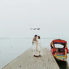 An intimate moment on a quiet dock in Kashmir, with birds flying overhead against a misty, minimalist landscape. This image captures the serene, fairytale-like atmosphere of our destination pre-wedding shoots.