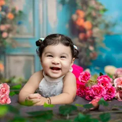 A happy baby girl with the cutest pigtails, lying in a field of flowers. Her joyful expression is the focus of this colorful portrait.