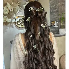 A beautiful and intricate hairstyle for a special occasion. This look features long, flowing curls decorated with fresh baby's breath flowers and a bow made of hair.