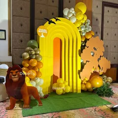 A vibrant photo booth corner with a "Hakuna Matata" sign. The setup includes a life-sized Mufasa cutout and a sunny yellow arch, perfect for capturing memories.
