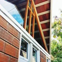 A close-up detail of a climate-responsive roof structure. The design uses a combination of exposed brick, a wooden frame, and clerestory windows to allow hot air to escape and daylight to enter, naturally cooling and lighting the space within.