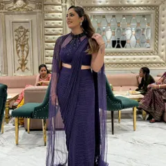 Make a statement with this modern purple drape saree. It comes with a stylish high-neck blouse and a flowing cape, giving you an elegant and contemporary look for any cocktail party or reception.