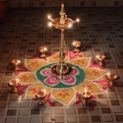 A traditional brass lamp, or 'Kuthu Vilakku', surrounded by small diyas on a colorful rangoli. This is how we celebrate Karthigai Deepam, the festival of lights.