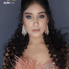A close-up portrait focusing on the soft smokey eye and nude lip combination. The voluminous curly hair complements the modern, feathered gown.