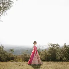 A breathtaking wide-angle bridal portrait. The bride stands alone against a vast, hazy landscape, creating a sense of serene beauty and epic scale.
