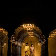 A wide shot of a couple in a grand, golden-lit hall, emphasizing the scale and opulence of the location.