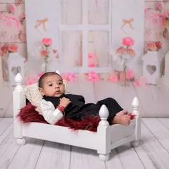 A wider view of the setup, showing the baby relaxing on the miniature bed. The floral background adds a soft and dreamy touch to the portrait.