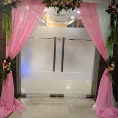 An elegant entrance decoration for a Roka ceremony, using pink and white drapes with floral arrangements to welcome guests.