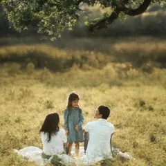 Seated on a blanket under a sprawling tree, the parents listen intently as their daughter tells a story. The golden hour light filters through the leaves, creating a magical atmosphere for this lifestyle family photography session.
