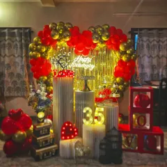 I design romantic setups to celebrate your special milestones together. This 35th anniversary decoration features a heart-shaped balloon arch in bold red and chrome gold, set against a golden shimmer curtain. The package includes a 'Happy Anniversary' neon sign, marquee numbers, and a variety of lit props like the 'LOVE' sign and a miniature tree to create a warm, intimate feel.