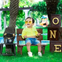 A happy one-year-old enjoying the sunshine in the park, with bright yellow sunglasses adding a fun touch.