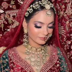 A beautiful bride wearing a unique chandbali-style Polki necklace set against a rich red and green velvet lehenga. The intricate details of the jewellery shine in this close-up.