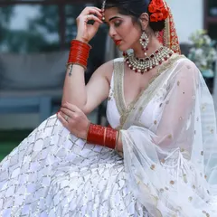 A beautiful and serene bridal portrait. The contrast between the white lehenga and the traditional red jewelry and flowers is timeless and elegant.