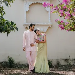 A romantic portrait of the couple at their Welcome Lunch. The groom's pastel pink embroidered jacket and the bride's sage green floral saree create a soft, coordinated, and elegant look.