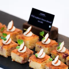 Our wild raspberry lemon almond cake, served as bite-sized canapés at a polo match high tea. These little squares are moist, flavourful, and elegantly garnished with an almond slice and microgreens.