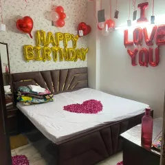 A perfect setup for celebrating a birthday with your special someone. This room decoration combines 'Happy Birthday' and 'I LOVE YOU' foil balloons with red and white ceiling balloons and a heart made of rose petals on the bed.