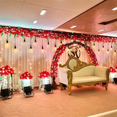 An elegant reception stage setup inside a banquet hall. We used a backdrop of white curtains with a red floral arch, accented with hanging Edison bulbs for a modern touch.