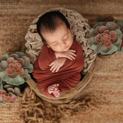 This little one is nestled in a woven basket and wrapped in a rich, earthy-toned swaddle. I use natural textures and props to create artistic and cozy newborn portraits.