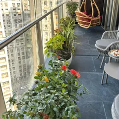 A long-shot of a balcony garden filled with a mix of flowering bushes and leafy plants, with modern outdoor furniture for enjoying the view.