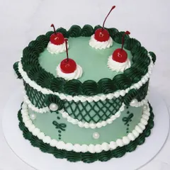 We're obsessed with the charm of vintage Lambeth cakes, and this one is a favorite. The intricate piping in forest green and white, topped with classic maraschino cherries, shows our dedication to this beautiful, ornate cake decorating style.