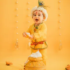 A classic studio portrait for Janmashtami. The bright yellow dhoti, peacock feather crown, and a happy, messy face make for an unforgettable photo.