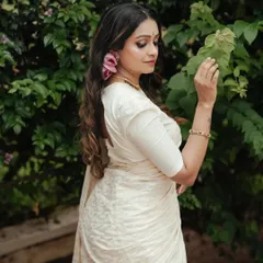 A side profile from the Onam series, highlighting the elegant drape of the saree and the intricate details of her hair and jewelry. The natural setting adds a soft, organic feel.